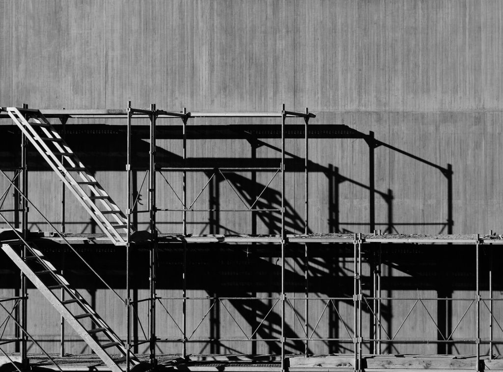 Steel scaffold with ladders beside a concrete wall. 